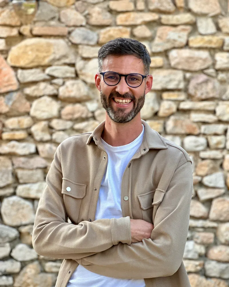Benoît Schrub, sourire et bras croisés devant un mur en pierres sèches